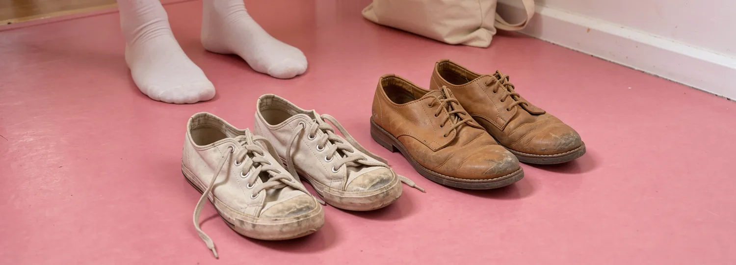 Two everyday shoes with their laces left loose on a pink hallway floor, with socks and a canvas bag nearby.